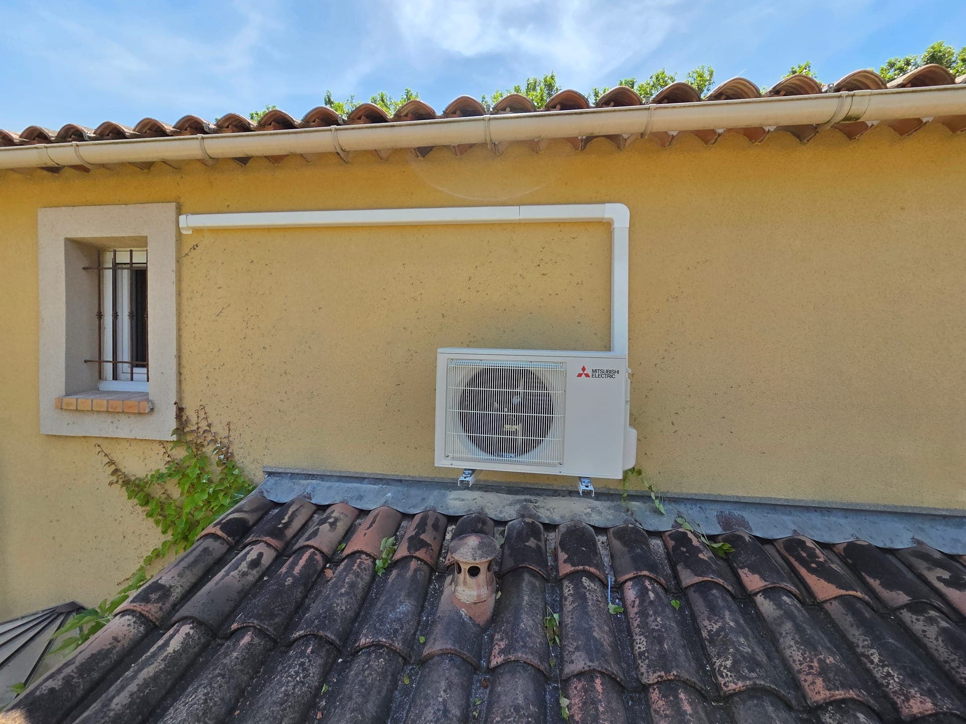 Groupe extérieur Mitsubishi sous débord de toiture en tuiles provençales — climatisation Miramas, plaine de la Crau